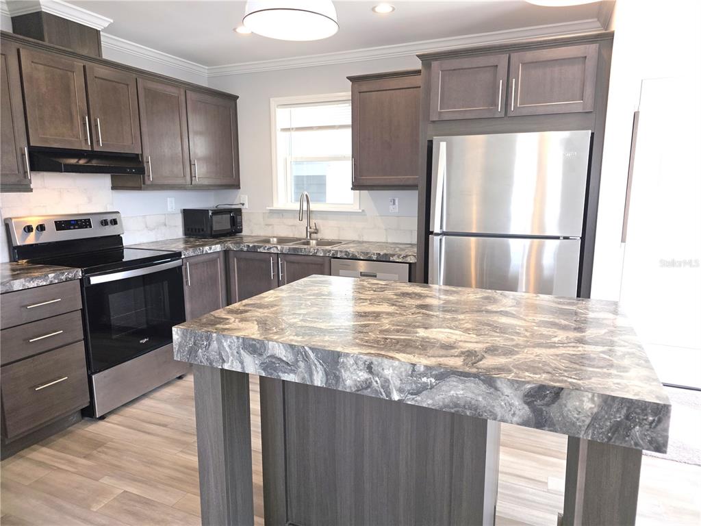 A kitchen features dark wood cabinets, a marble-patterned island, and stainless steel appliances — 236 WOLVERINE AVENUE, NORTH PORT, FL