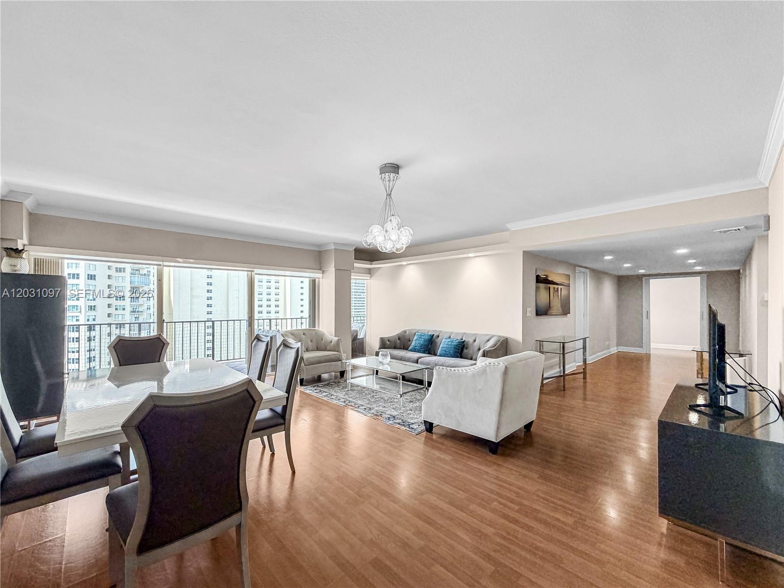 A spacious living and dining area features hardwood floors, a modern chandelier, and balcony access — 1800 NE 114th St # 1607, Miami FL 33181, MIAMI, FL