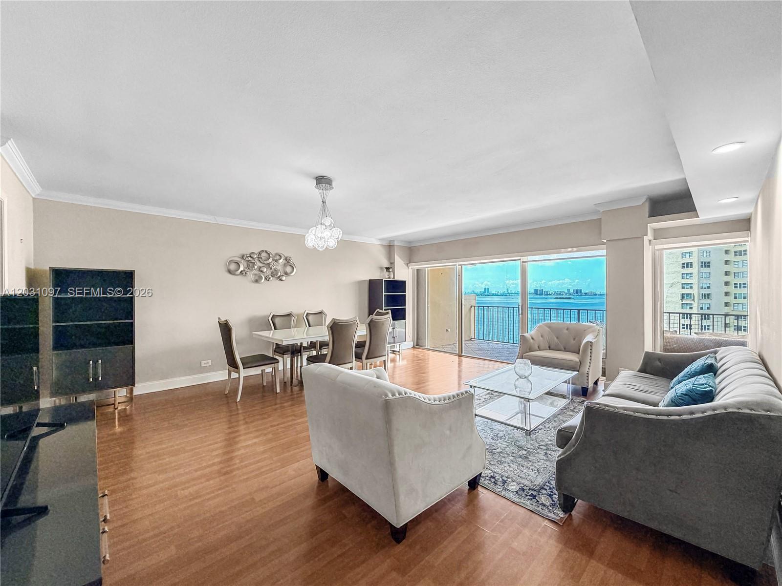 A living and dining area features hardwood floors, modern furniture, and a balcony with water views — 1800 NE 114th St # 1607, Miami FL 33181, MIAMI, FL