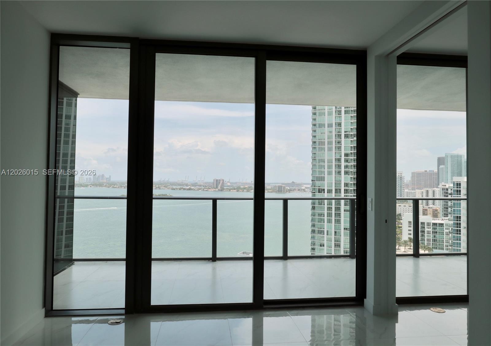 A room with floor-to-ceiling windows and a balcony overlooking a bay and city skyline — 650 NE 32 # 1906, Miami FL 33137, MIAMI, FL