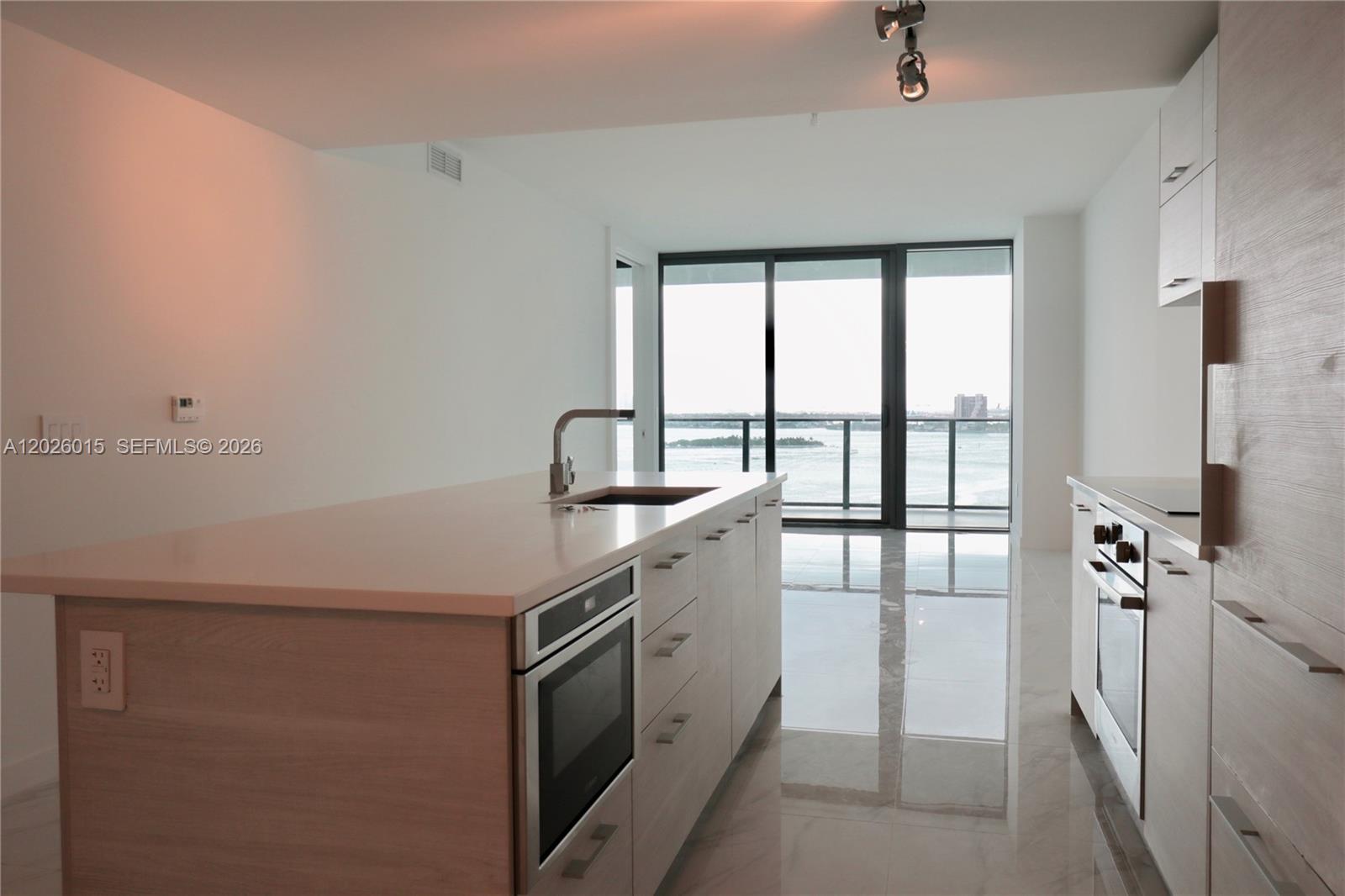 A modern kitchen features light wood cabinetry, a central island with a sink, and floor-to-ceiling windows — 650 NE 32 # 1906, Miami FL 33137, MIAMI, FL