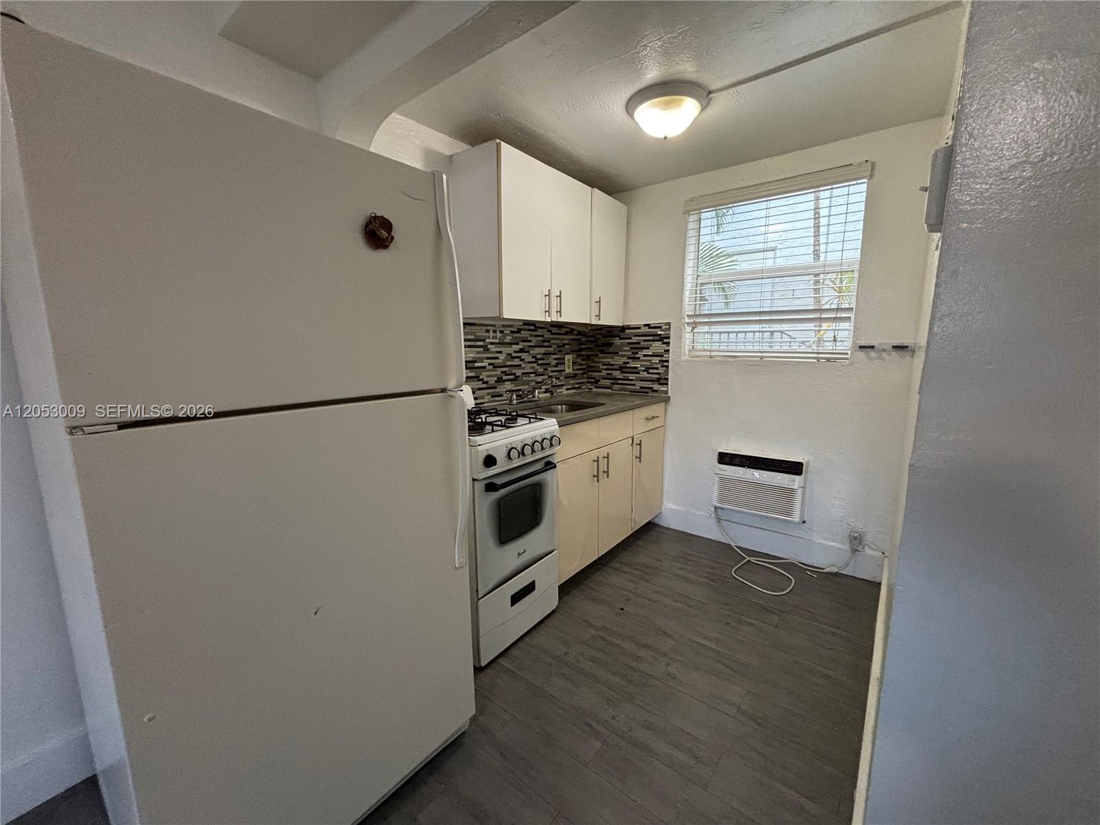 A small kitchen features white cabinets, a gas stove, a refrigerator, and wood-look flooring — 1843 Dewey St # 121, Hollywood FL 33020, HOLLYWOOD, FL