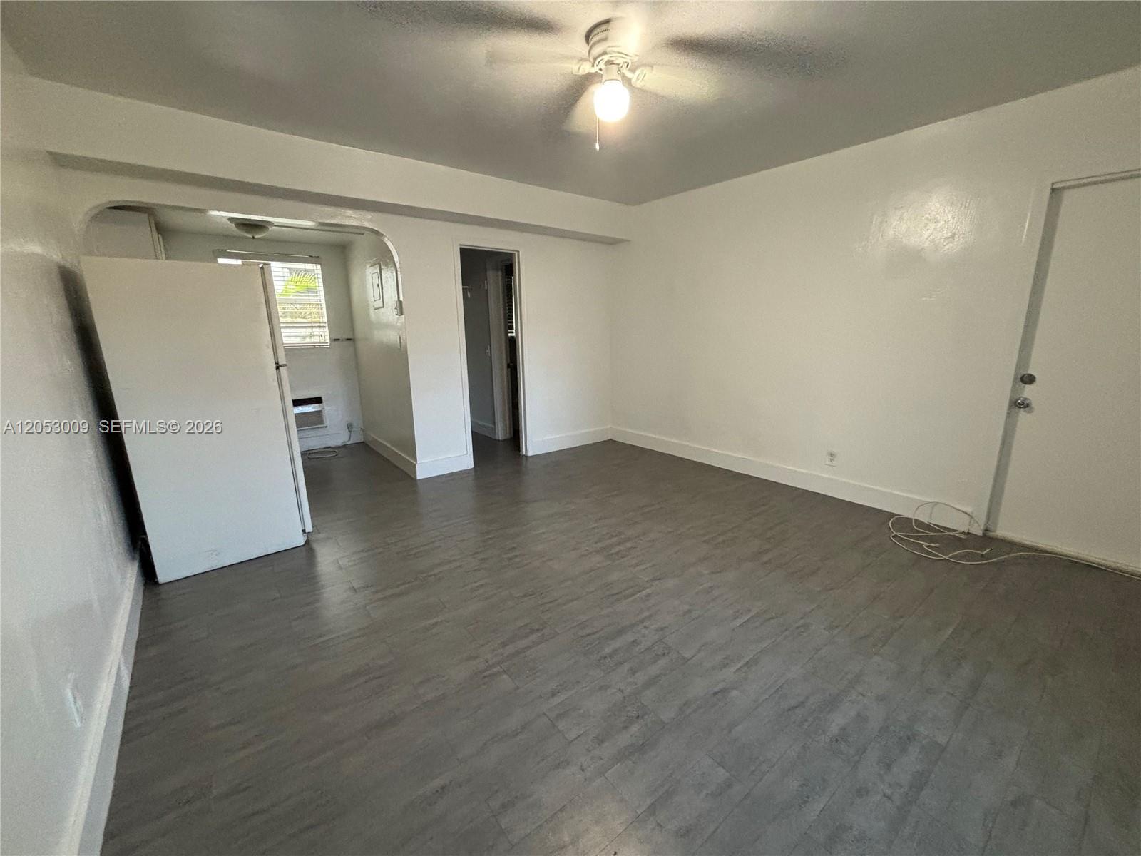 An unfurnished room features gray wood-look flooring, white walls, a ceiling fan, and a refrigerator — 1843 Dewey St # 121, Hollywood FL 33020, HOLLYWOOD, FL