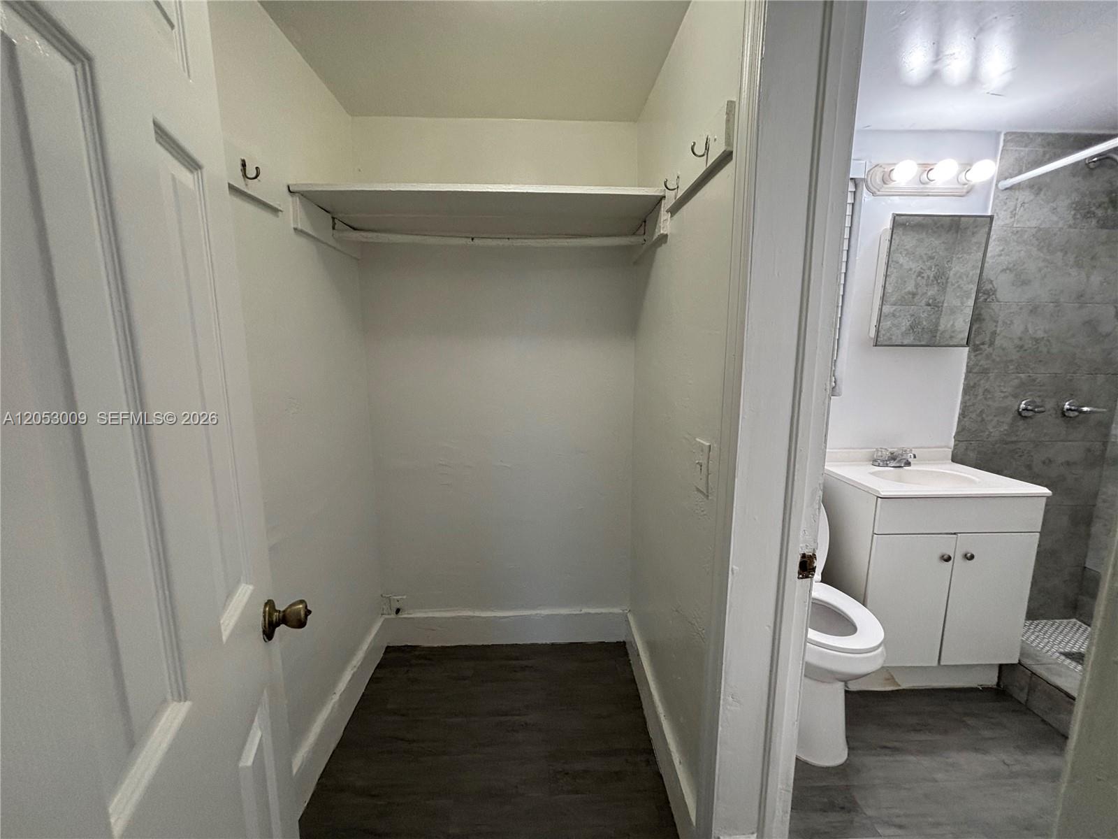 A small closet with a single shelf and hooks sits adjacent to a bathroom — 1843 Dewey St # 121, Hollywood FL 33020, HOLLYWOOD, FL