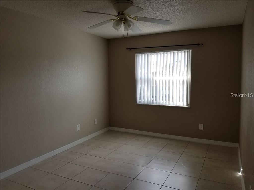An empty bedroom features beige walls, a ceiling fan, and light-colored tile flooring — 2417 BARLEY CLUB COURT UNIT 6, ORLANDO, FL