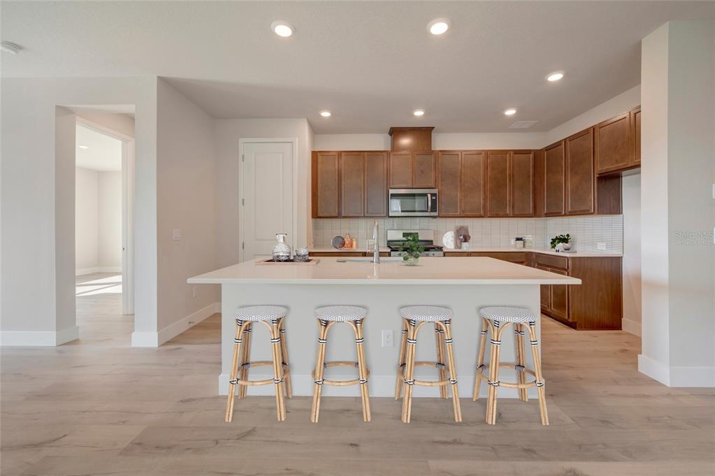 A kitchen features a large white island with four stools, wood cabinets, and light flooring — 5152 CREEK SAND DRIVE, APOLLO BEACH, FL