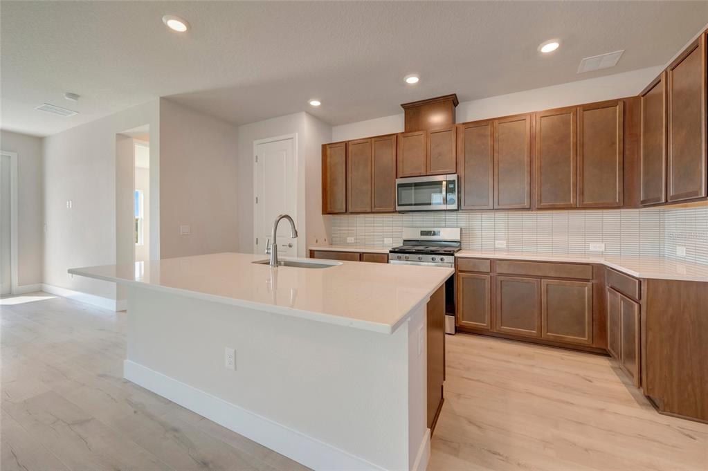 A kitchen features dark wood cabinets, a white quartz island with a sink, and light flooring — 5152 CREEK SAND DRIVE, APOLLO BEACH, FL