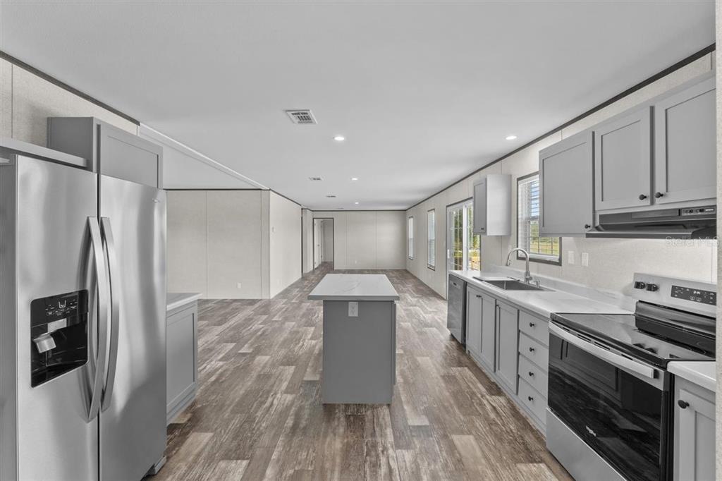 A kitchen with grey cabinets, stainless steel appliances, a central island, and wood-look flooring — 8457 N CAROUSEL TERRACE, CRYSTAL RIVER, FL