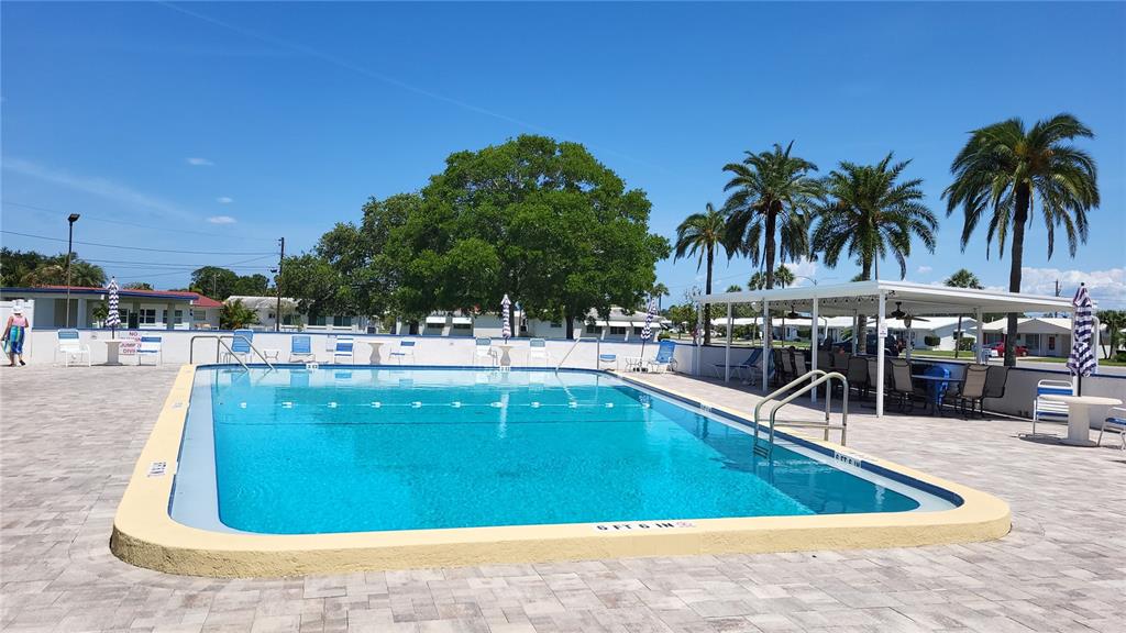 A rectangular outdoor swimming pool is surrounded by a paved deck with palm trees nearby — 9660 44TH STREET N, PINELLAS PARK, FL
