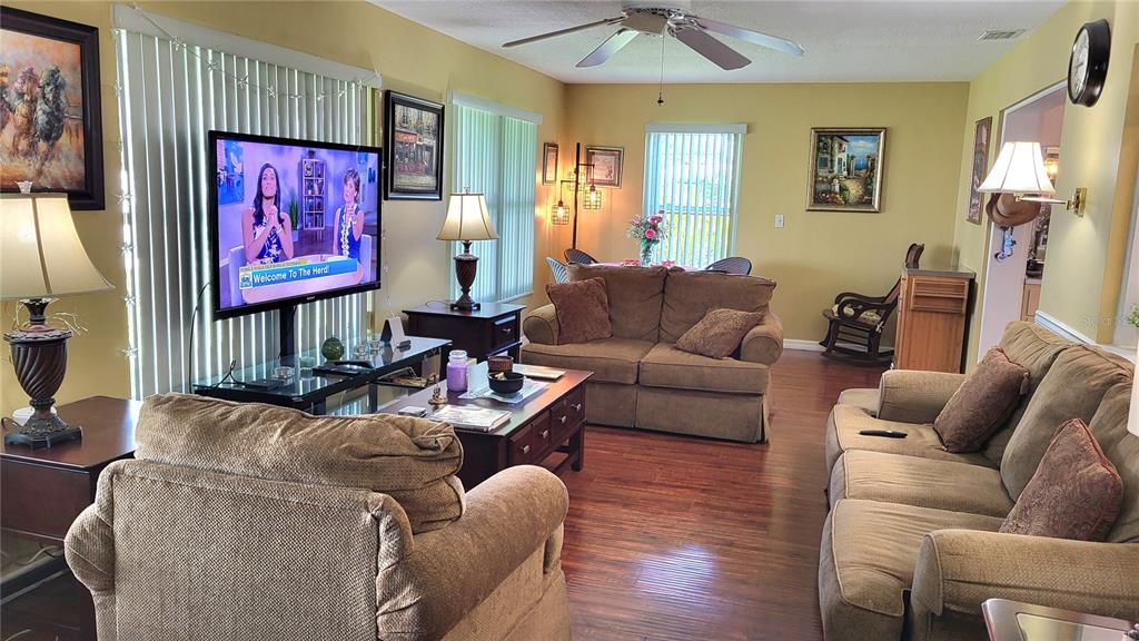 A living room features brown sofas, a television, a coffee table, and wood-look flooring — 9660 44TH STREET N, PINELLAS PARK, FL