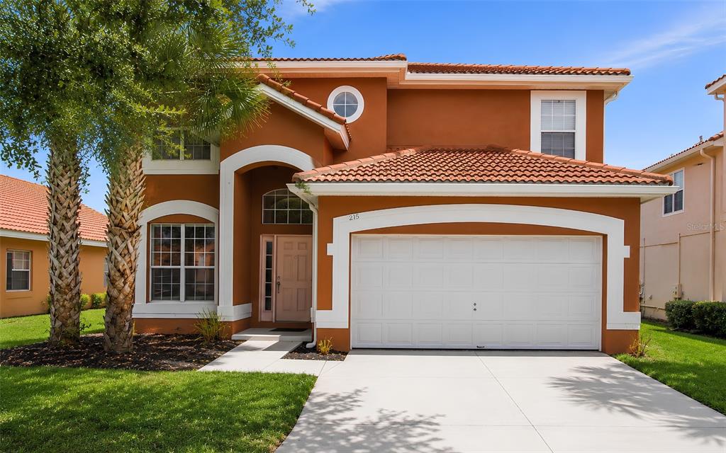 A two-story house with orange stucco walls, a white garage door, and a tiled roof — 216 SEVILLA AVENUE, DAVENPORT, FL
