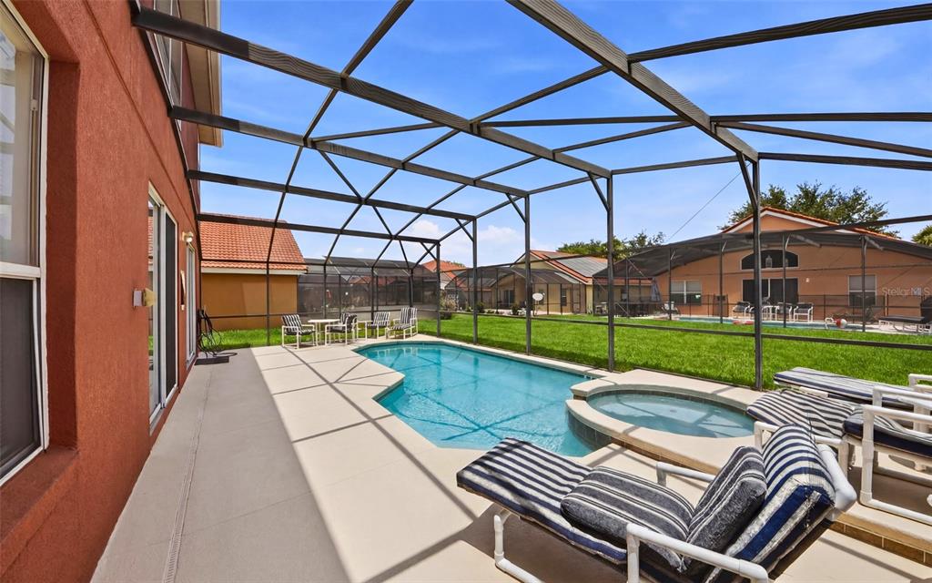 A screened-in pool and spa area with lounge chairs on a concrete patio — 216 SEVILLA AVENUE, DAVENPORT, FL