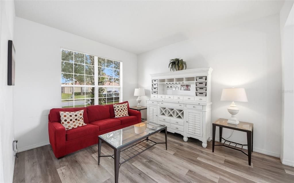 A living room features a red sofa, glass coffee table, and white hutch on wood-look flooring — 216 SEVILLA AVENUE, DAVENPORT, FL