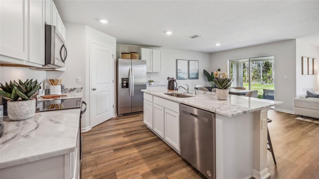 A dining area with a wooden table and white chairs sits beside a modern kitchen — 5814 SILVER MOONLIGHT DRIVE, PALMETTO, FL