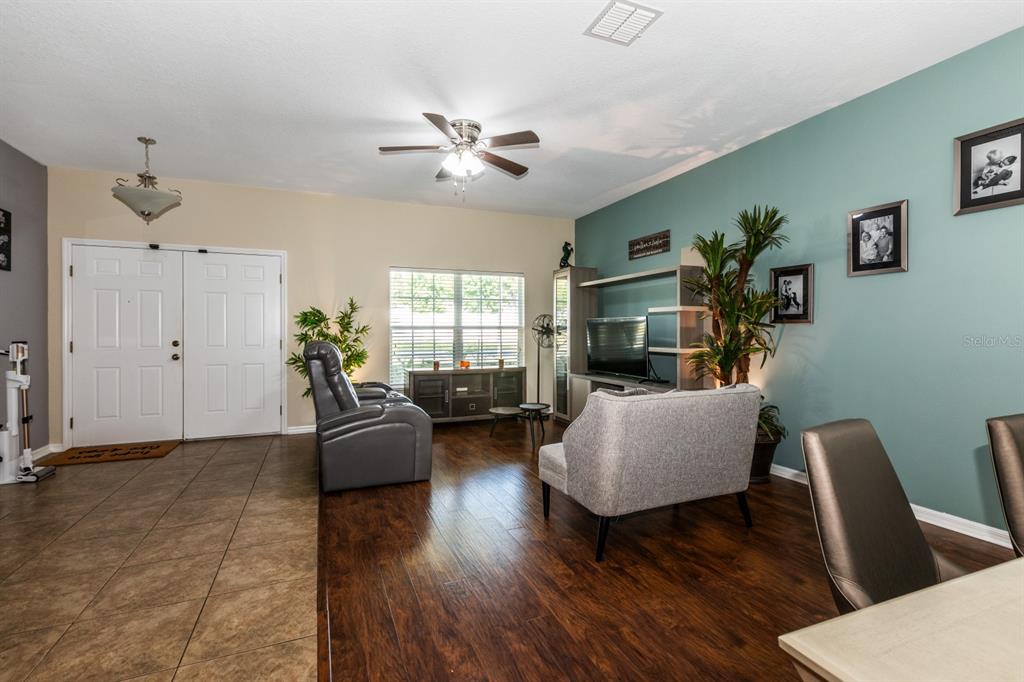 A living room features a gray sofa, a recliner, a television console, and wood flooring — 2943 ETOWAH PARK BOULEVARD, TAVARES, FL