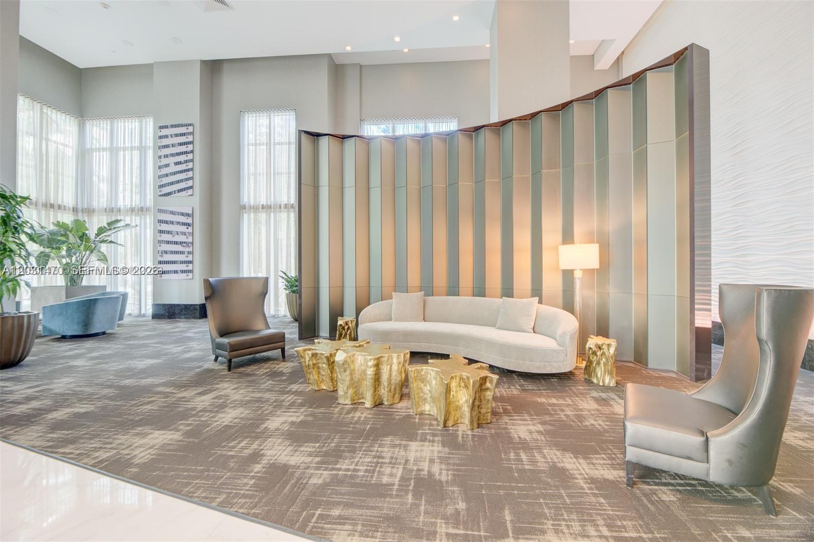 A modern lobby features a curved sofa, gold stump tables, and a tall metallic partition — MIAMI, FL