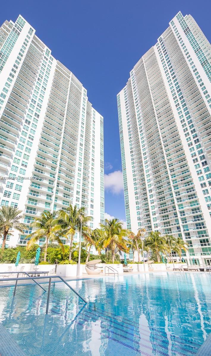 A swimming pool sits in front of two tall, white residential high-rise buildings — MIAMI, FL