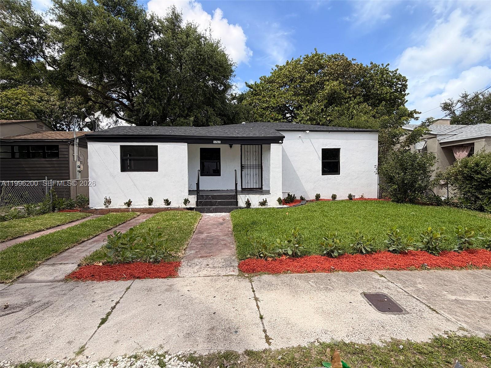 A single-story white house with a black roof and a front porch sits behind a lawn — 1261 NW 45th St, Miami FL 33142, MIAMI, FL