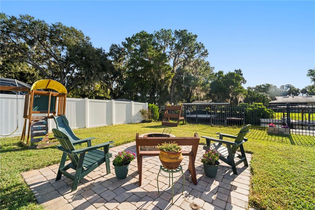 A backyard features a brick patio with a fire pit, two chairs, and a playset — 35638 CALLA COURT, LEESBURG, FL
