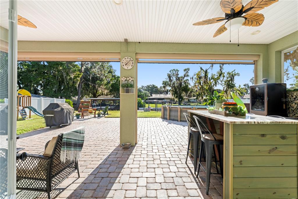 A covered brick patio features a bar with stools, a ceiling fan, and a backyard view — 35638 CALLA COURT, LEESBURG, FL