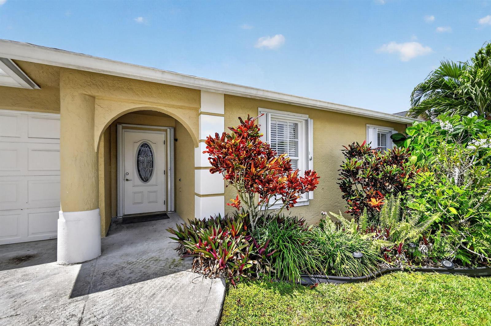 A tan house exterior features a white front door, arched entryway, and colorful landscaping — 1080 Salmon Isle, FL 33413, FL