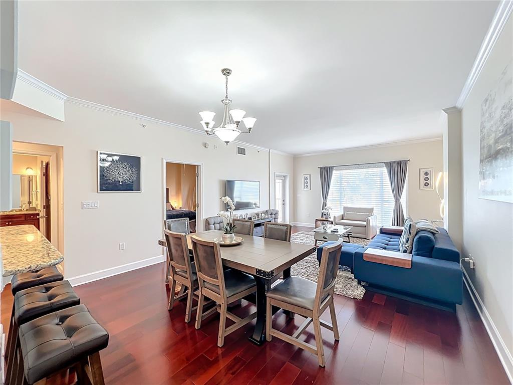 An open-concept living and dining area features dark wood floors, a blue sofa, and chandelier — 2305 EDGEWATER DRIVE UNIT 1404, ORLANDO, FL