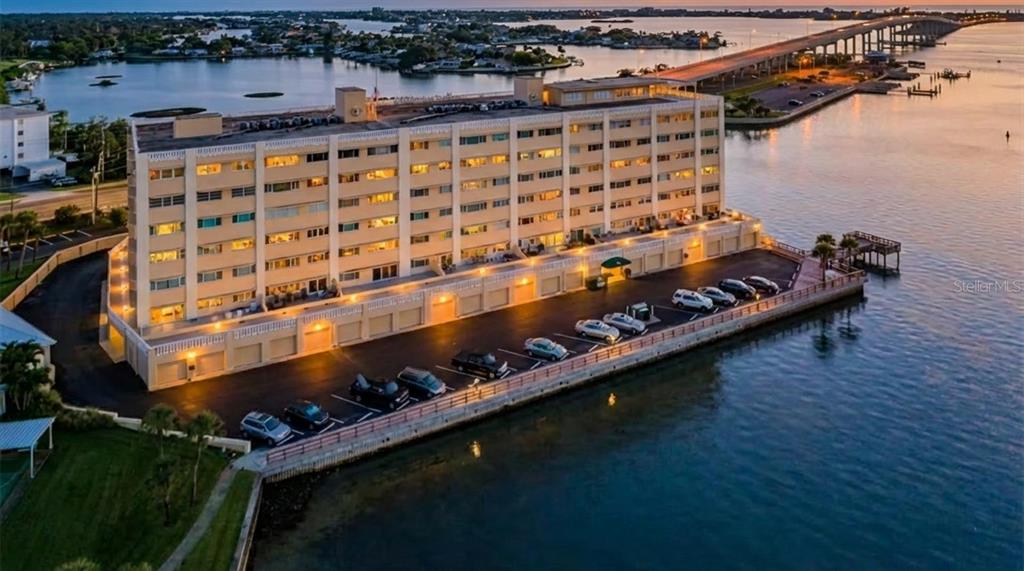 An aerial view shows a multi-story apartment building situated on a waterfront lot with parking — 100 BLUFF VIEW DRIVE UNIT 211C, BELLEAIR BLUFFS, FL