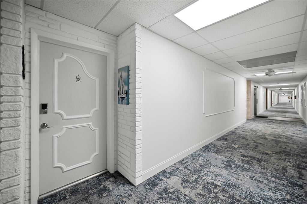 A long, carpeted apartment hallway features a white door with decorative molding and brick accents — 100 BLUFF VIEW DRIVE UNIT 211C, BELLEAIR BLUFFS, FL