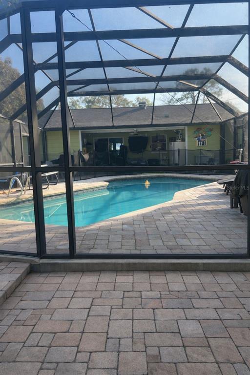 A screened-in patio features a swimming pool surrounded by light-colored stone pavers — 4912 E SERENA DRIVE, TAMPA, FL