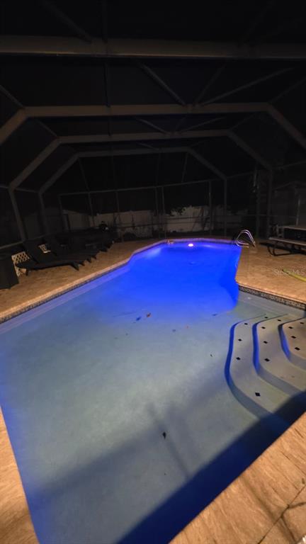 A swimming pool with blue underwater lighting sits inside a screened-in lanai at night — 4912 E SERENA DRIVE, TAMPA, FL