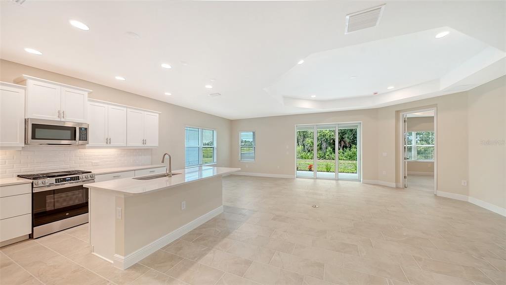 A modern kitchen with white cabinets and a center island opens into a spacious living area — 6547 BIG BAYOU DRIVE, SARASOTA, FL