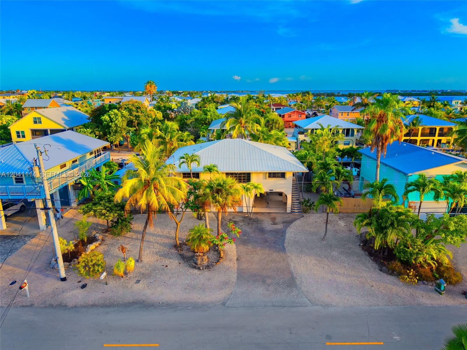 An elevated house with a metal roof stands behind a paved driveway and palm trees — BIG PINE, FL