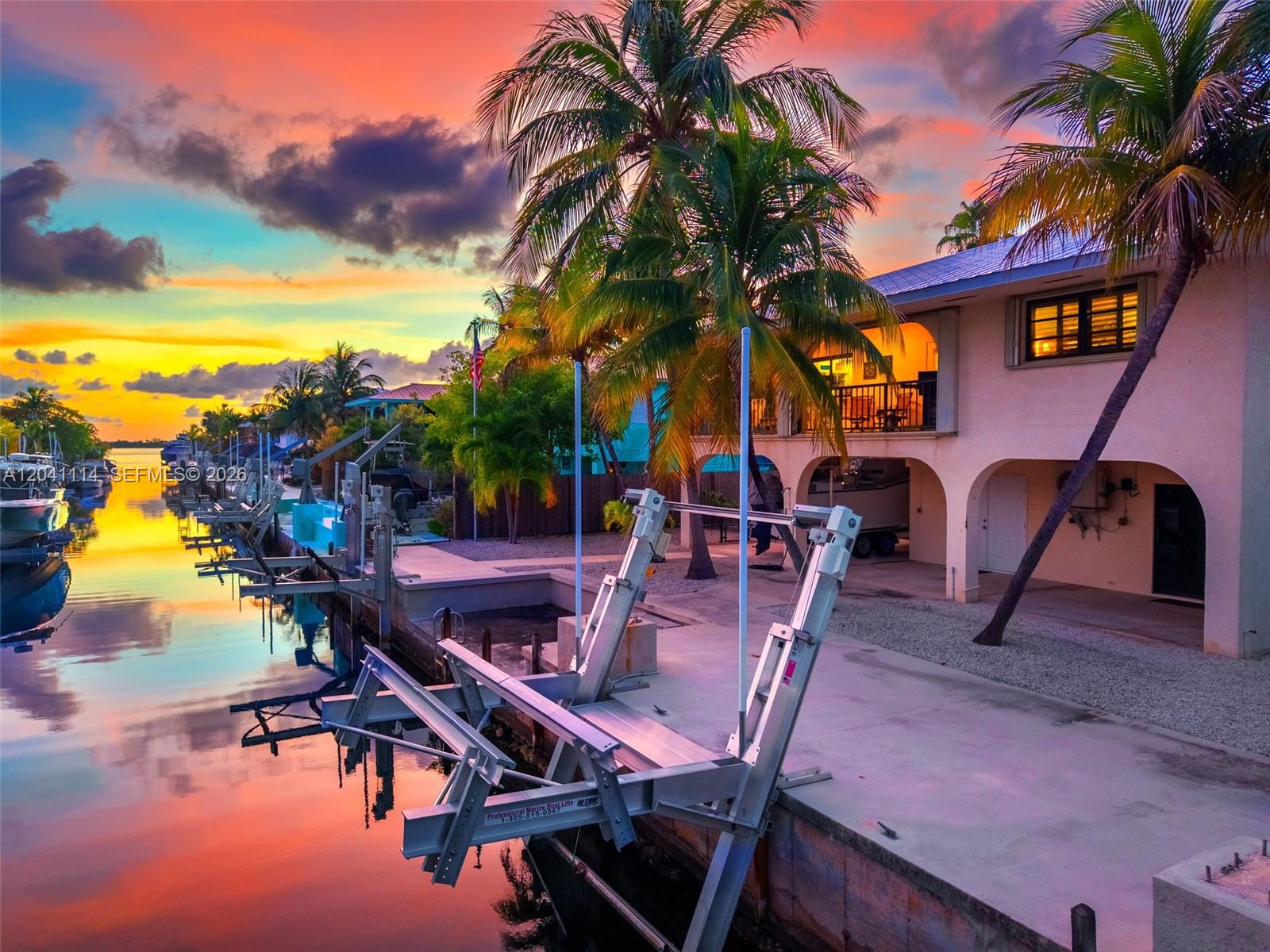 A waterfront house with a boat lift at sunset, featuring palm trees and a canal — BIG PINE, FL