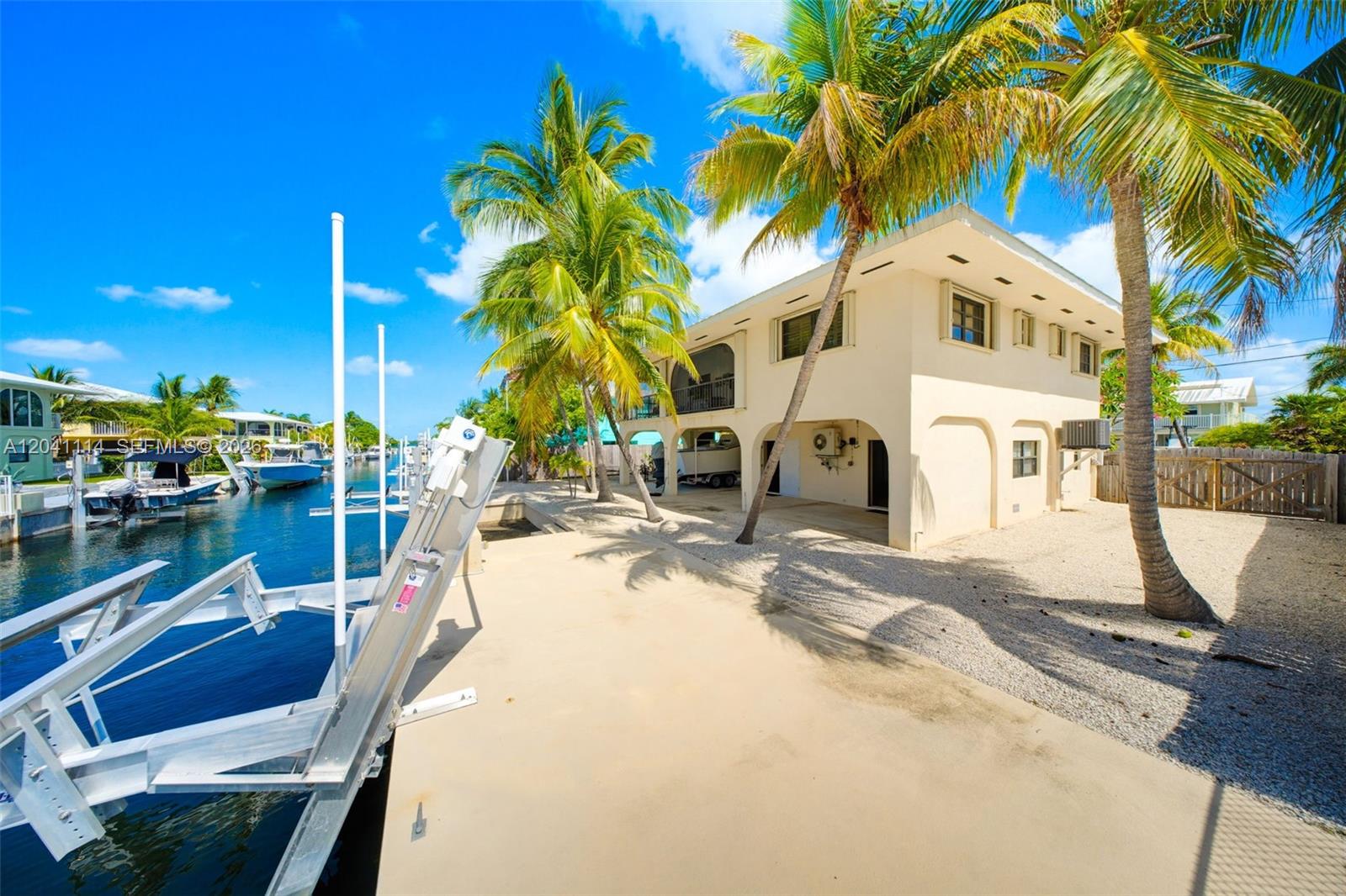A two-story house with a boat lift sits along a canal under palm trees — BIG PINE, FL