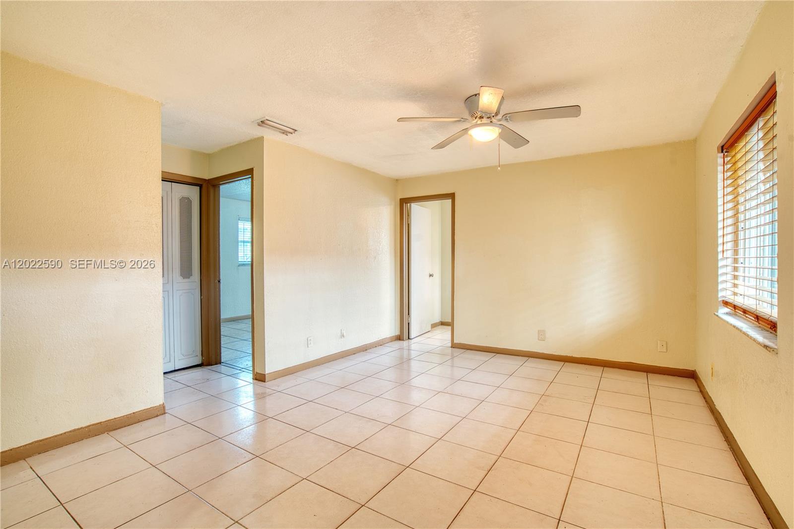 An empty room features light-colored tile flooring, beige walls, a ceiling fan, and two doorways — 129 SE 4th Ave # 1, Hallandale Beach FL 33009, HALLANDALE BEACH, FL