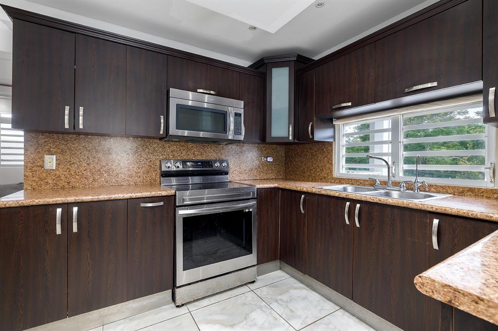 A kitchen features dark wood cabinets, granite countertops, stainless steel appliances, and white tiled floors — 843 SECT LOS RAMOS, TRUJILLO ALTO, PR
