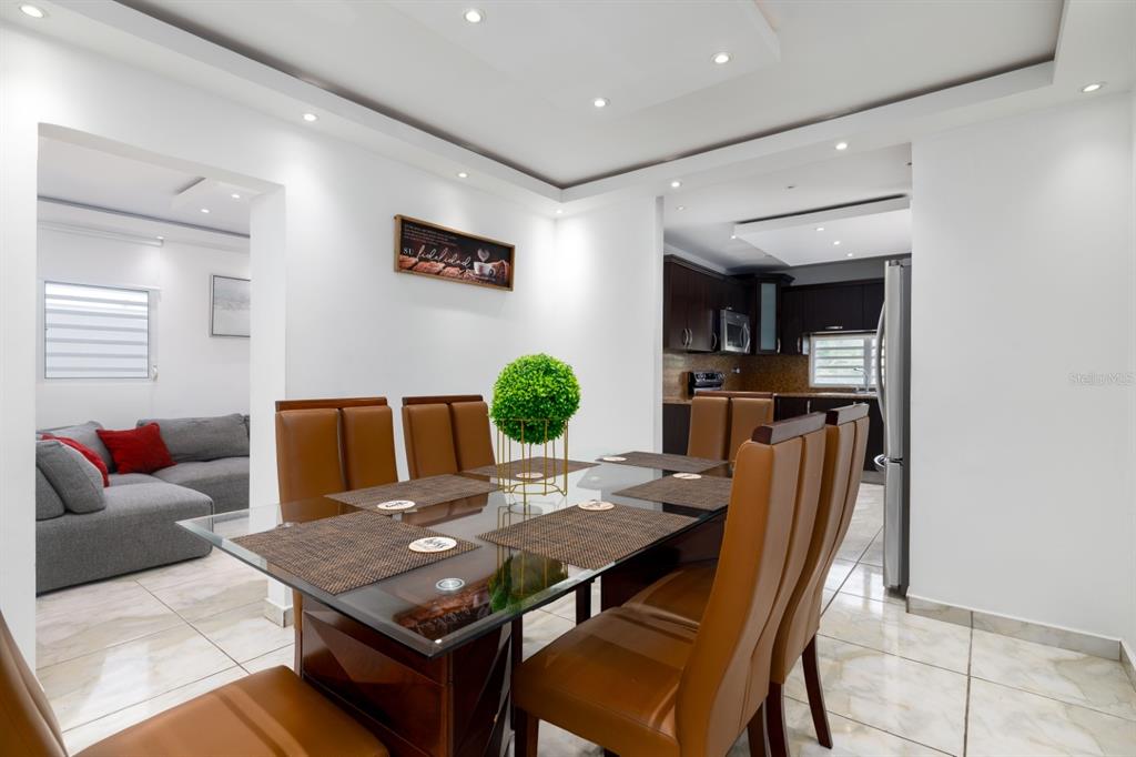 A dining room with a glass-topped table and brown chairs sits adjacent to a kitchen — 843 SECT LOS RAMOS, TRUJILLO ALTO, PR