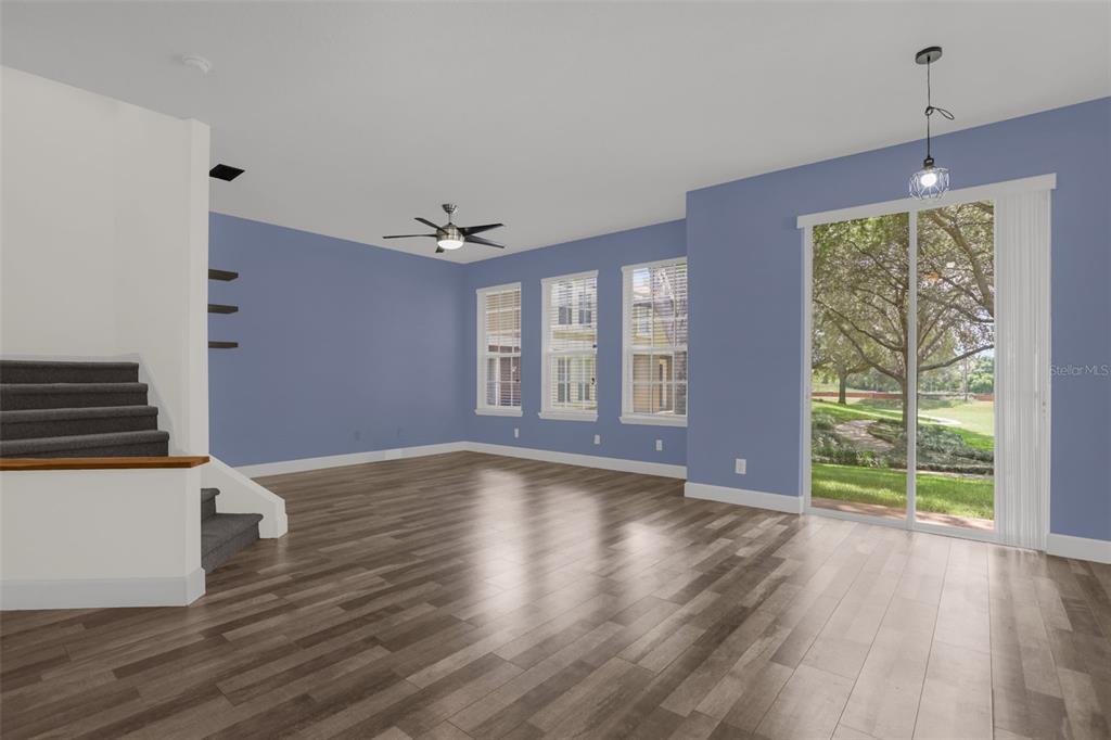 An empty living room with blue walls, wood-look flooring, a staircase, and sliding glass doors — 740 ASHWORTH OVERLOOK DRIVE UNIT B, APOPKA, FL