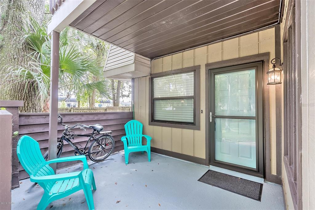A covered patio features two turquoise chairs, a bicycle, and a glass-paneled entry door — 3656 JACKSON STREET UNIT 10, PORT ORANGE, FL