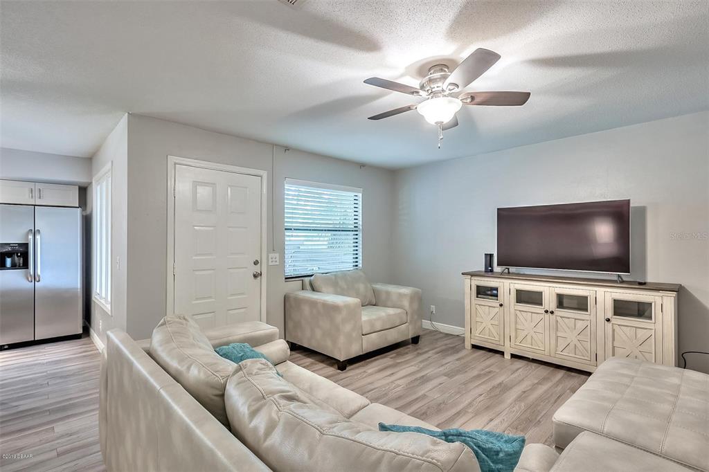 A living room features a sectional sofa, an armchair, a television console, and wood-look flooring — 3656 JACKSON STREET UNIT 10, PORT ORANGE, FL