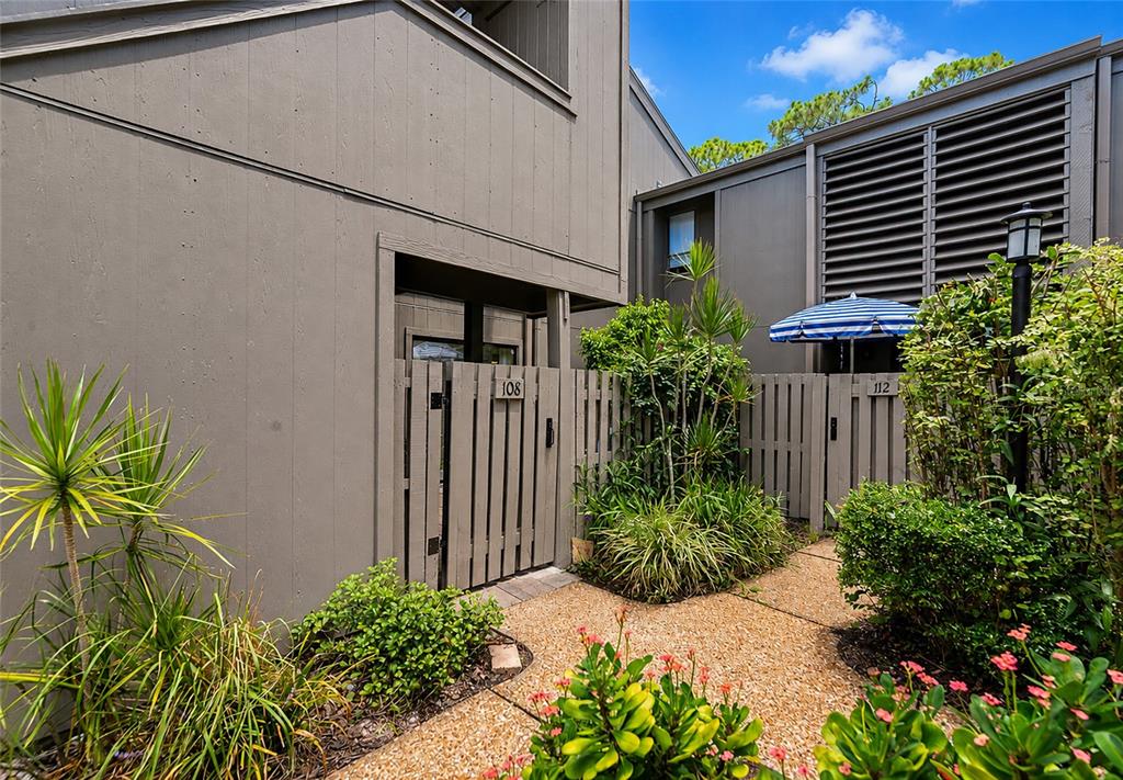 A view of two adjacent residential unit entrances with wooden gates and landscaping — 108 WOODLAND PLACE UNIT 108, OSPREY, FL