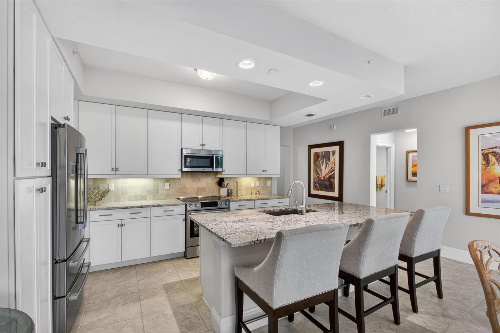 A kitchen features white cabinetry, granite countertops, a center island with seating, and stainless appliances — 834 Bay Colony Drive S, Juno Beach FL 33408, JUNO BEACH, FL