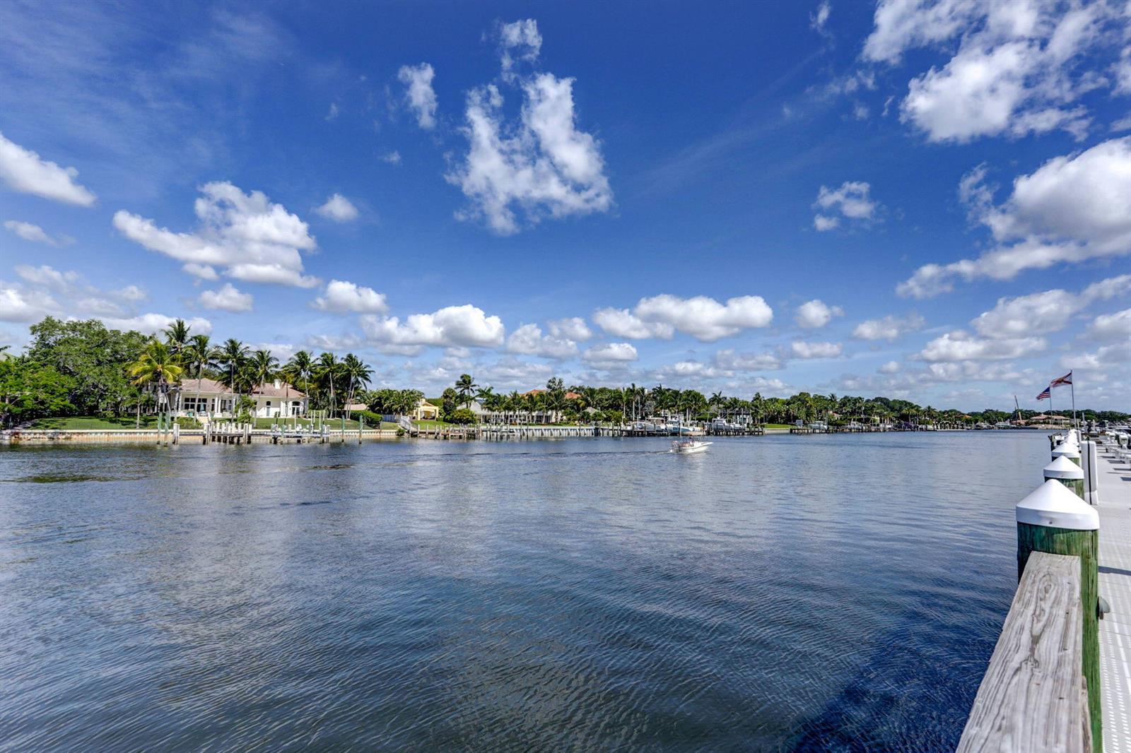A view from a wooden dock looking across a canal toward waterfront houses and palm trees — 834 Bay Colony Drive S, Juno Beach FL 33408, JUNO BEACH, FL