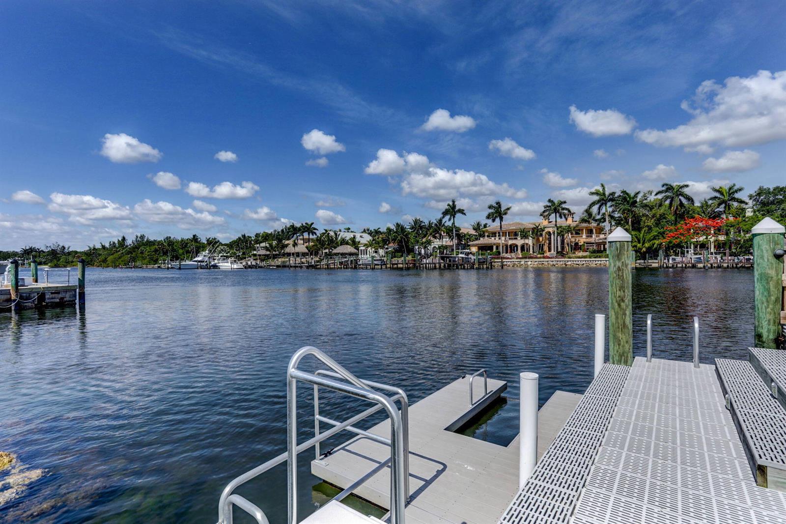 A view from a metal dock looking across a canal toward waterfront houses and palm trees — 834 Bay Colony Drive S, Juno Beach FL 33408, JUNO BEACH, FL