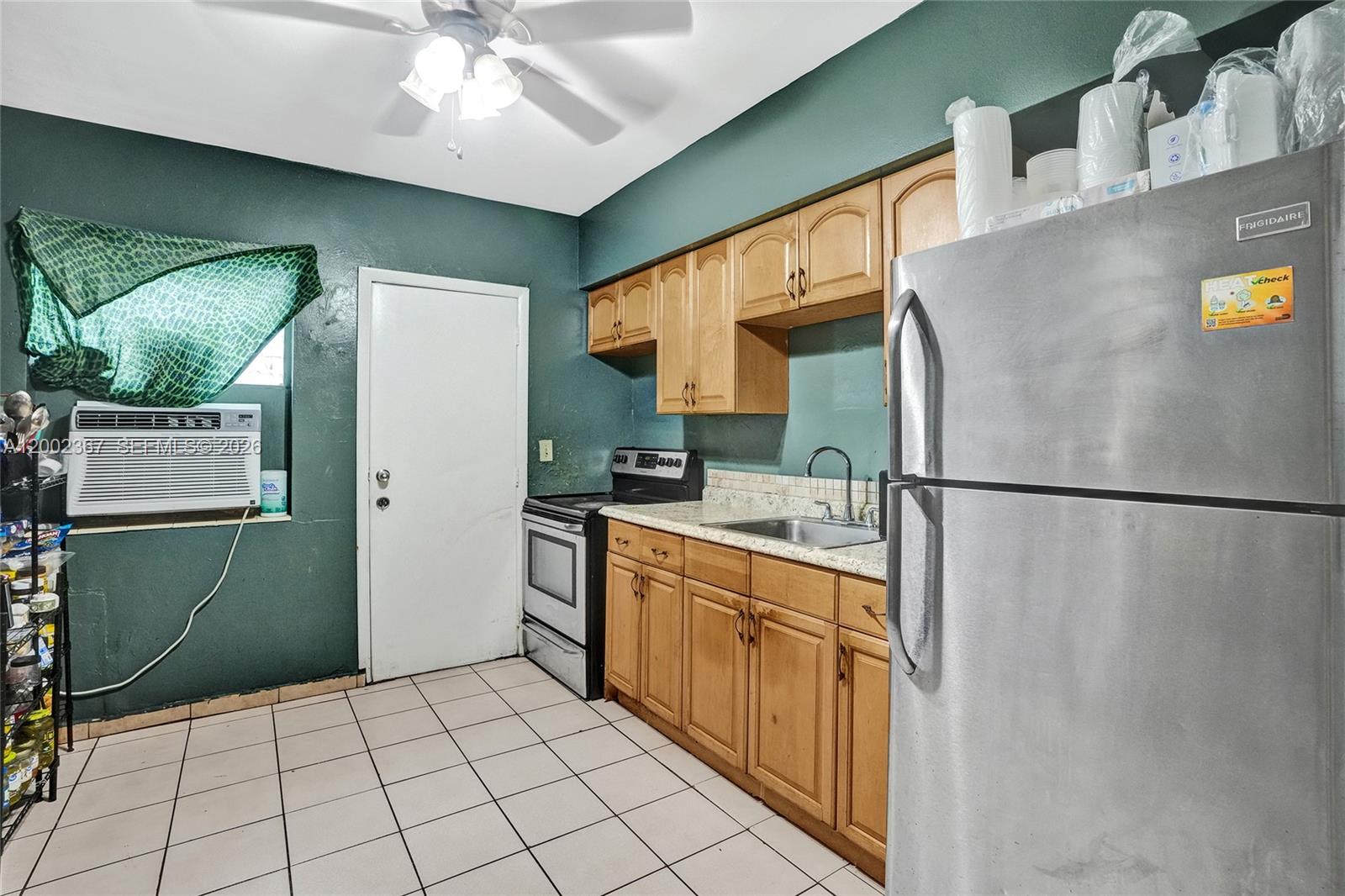 A kitchen features dark green walls, wooden cabinets, stainless steel appliances, and white tile flooring — 836 NW 101st St, Miami FL 33150, MIAMI, FL