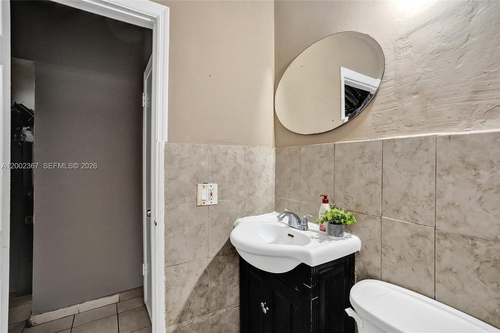 A bathroom features a small black vanity, a white sink, and beige wall tiles — 836 NW 101st St, Miami FL 33150, MIAMI, FL