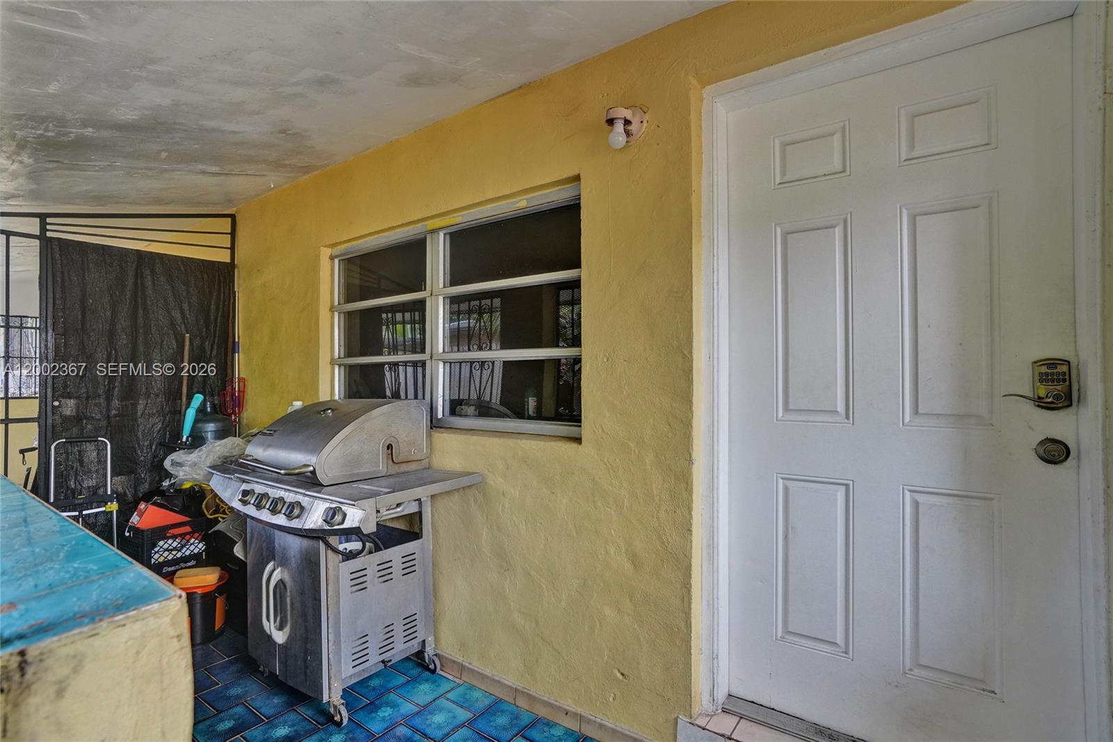 A covered patio features a yellow stucco wall, a white door, and a stainless steel grill — 836 NW 101st St, Miami FL 33150, MIAMI, FL