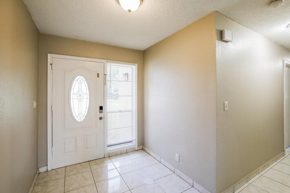 An entryway features a white front door with a glass insert, tile flooring, and beige walls — CORAL SPRINGS, FL