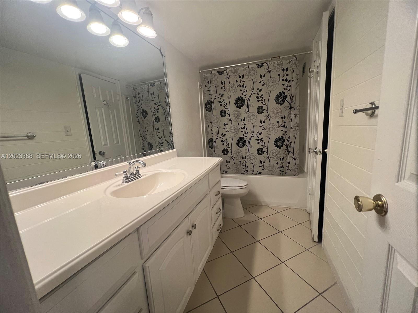 A bathroom features a white vanity, a floral shower curtain, and light-colored tile flooring — 2060 NW 48th Ter # 103, Lauderhill FL 33313, LAUDERHILL, FL
