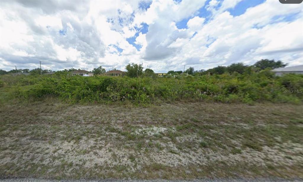 An overgrown, vacant lot with scattered shrubs and trees under a cloudy sky — 2707 64TH STREET W, LEHIGH ACRES, FL